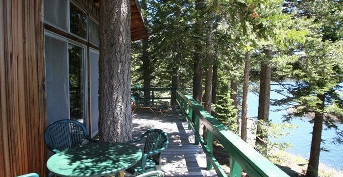 A cabin balcony with  railings offering a serene view of a lake through tall trees. - Kit Carson Lodge