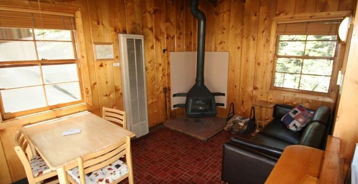 A cozy cabin interior with warm wood paneling and a dining table with chairs. - Kit Carson Lodge & Restaurant 
