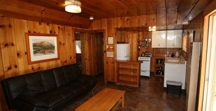 A cozy cabin interior features warm wood paneling, a leather couch and a kitchenette with cabinets - Kit Carson Lodge