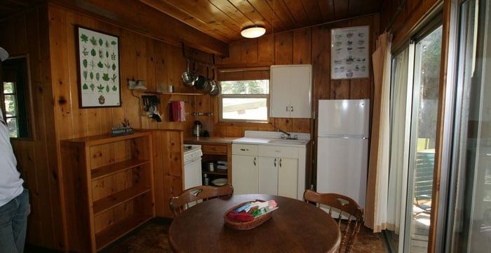 A rustic cabin interior with wood paneling and a round dining table with chairs. - Kit Carson Lodge & Restaurant 