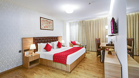 A wide-angle view of a premium guest room showing a bed with red pillows, light oak furniture, and elegant wall art - Hotel 91 HUDA City Centre, Gurugram