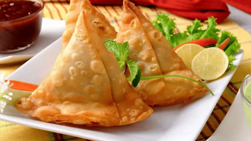 A plate of Shahi Samosa, elegantly arranged with fresh mint leaves, a wedge of lemon, and a spicy chili for a burst of flavour.