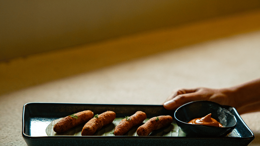 A person's hand reaches for a plate of appetisers and a small bowl of sauce at Stanley Revelation.