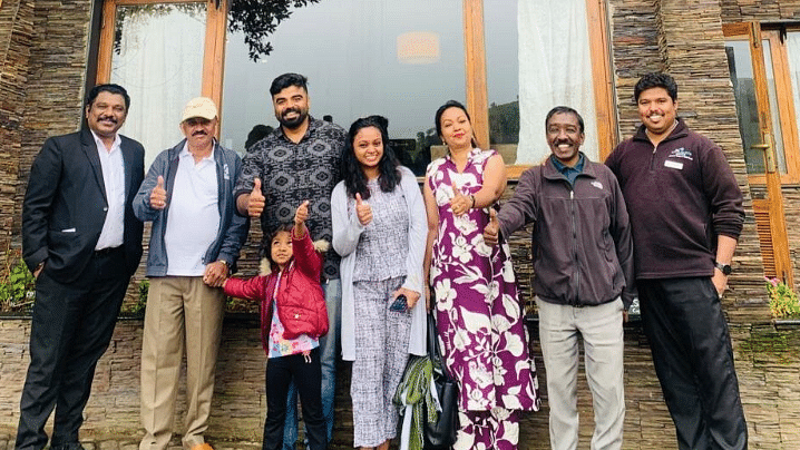 A cheerful group of adults and a child pose with thumbs up in front of the Destiny Farm Resort building. The wooden and stone façade of the resort, along with the sign above the balcony, creates a warm and welcoming backdrop.