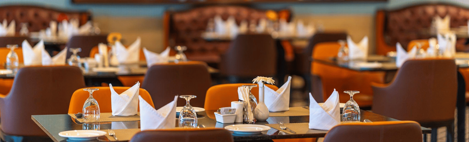 Cozy, contemporary restaurant interior with brown leather chairs, neatly set tables, and a large, colorful piece of abstract art on the wall.