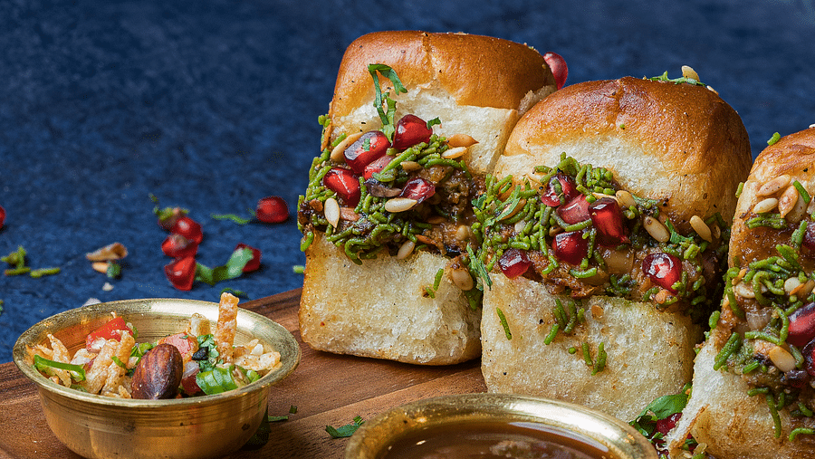 A picture of Dabeli filled with pomegranate and various toppings, accompanied by a bowl of sauce and another bowl of salad.