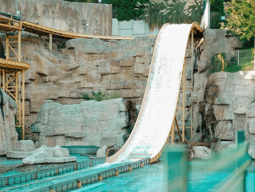 A slide dropping down to a waterbody at a water park with trees in the background