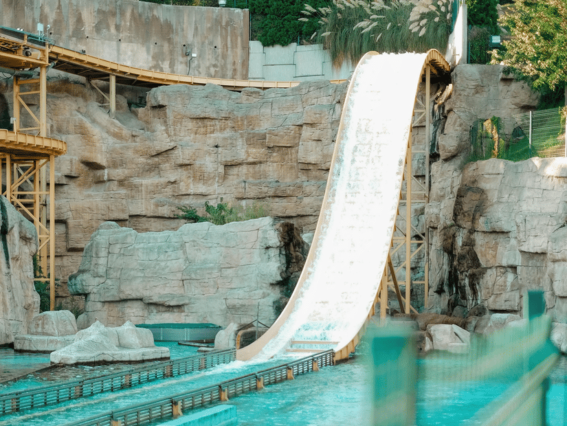 A slide dropping down to a waterbody at a water park with trees in the background