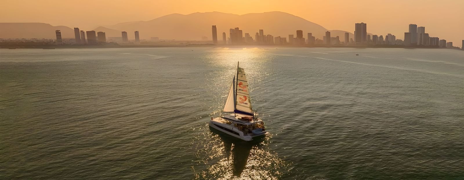 A serene boat cruise at sunset with panoramic views of the city skyline and calm sea, ideal for relaxing evenings at Alibu Resort.