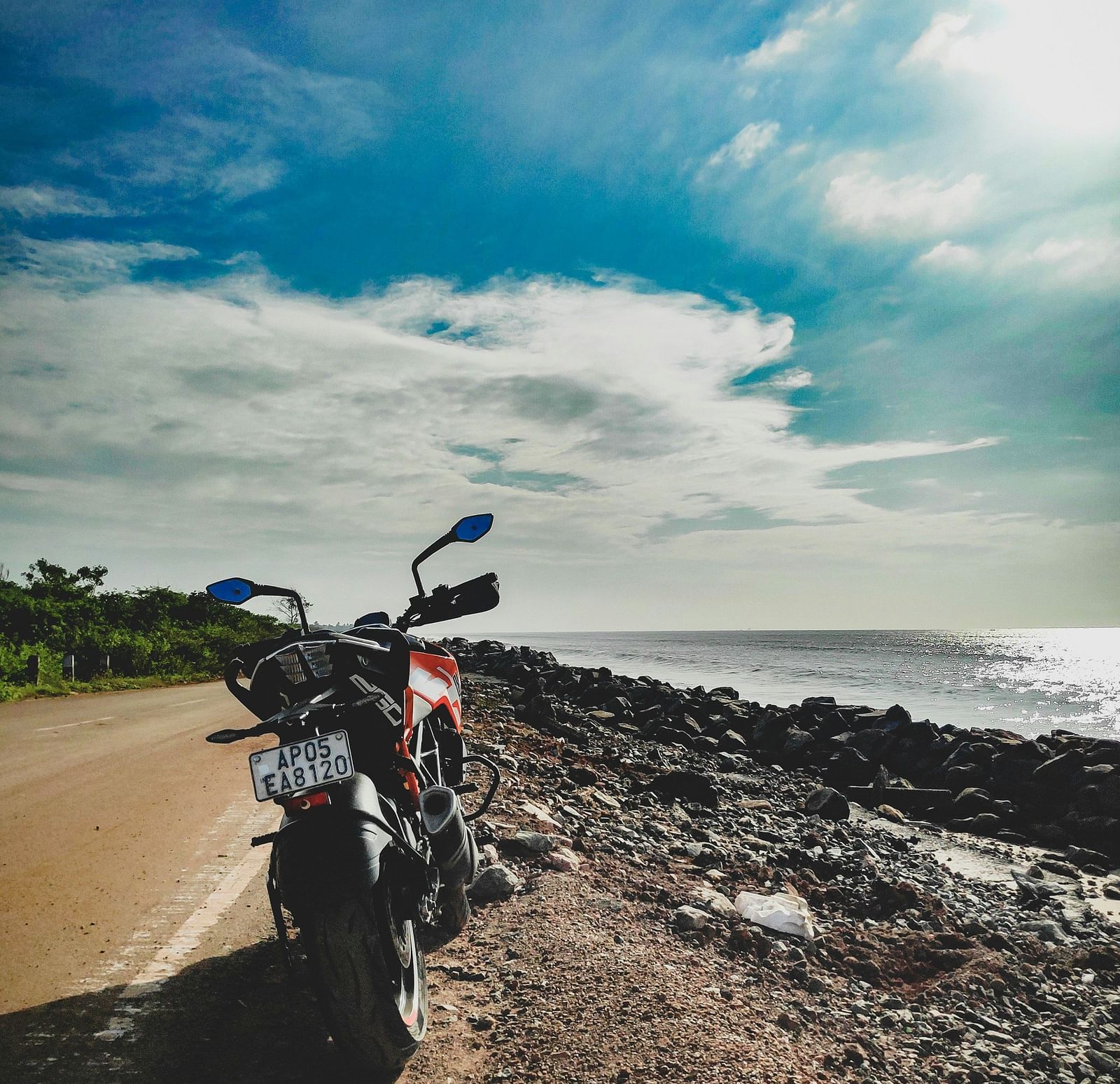 A bike parked near the beach with the sun and clouds in view