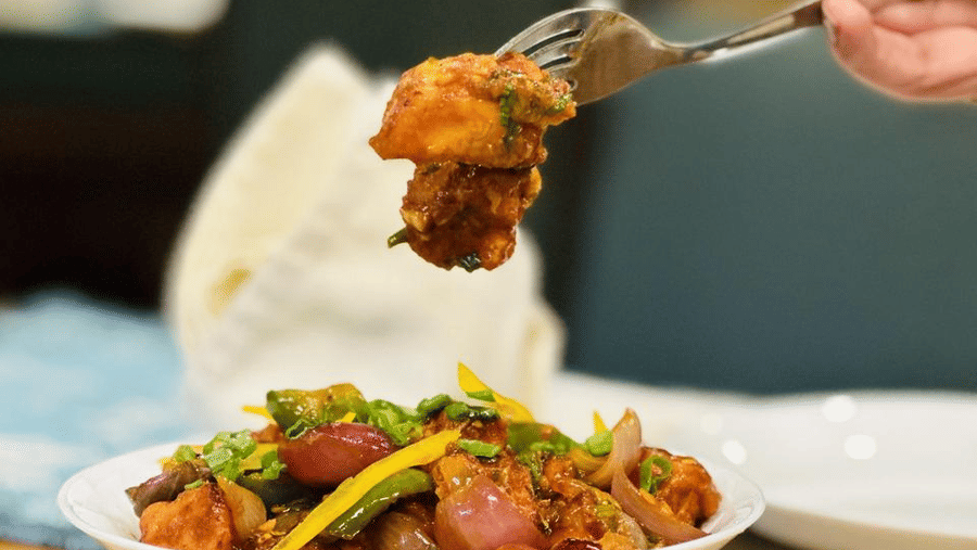 Close up of a person picking up a bite from a serving of an Indo-Chinese dish from a white porcelain bowl at Navidya Restaurant - Amantra Comfort Hotel