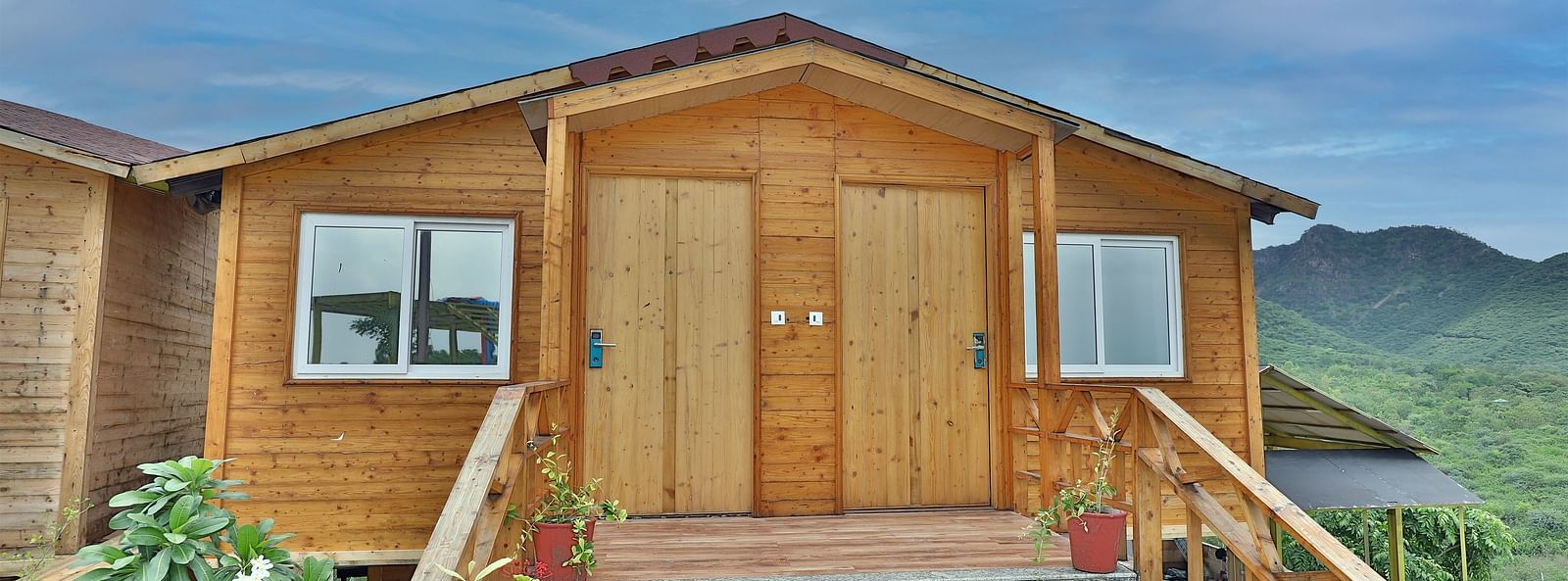 A wooden cabin with a porch and steps, set against a backdrop of mountains and a sky. - Bamboo Saa Resort & Spa, Udaipur