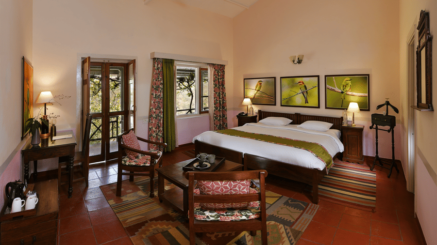 Premium bedroom with wooden bed seating area side tables and soft lighting offering comfort and space at Neemrana’s Glasshouse on The Ganges designed for extended and relaxing stays
