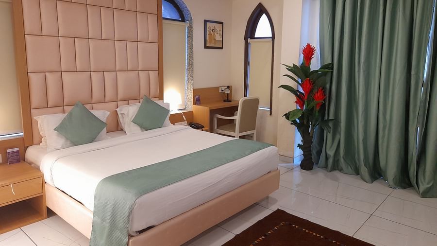 An elegant bedroom with a large bed, work desk & chair, and green curtains - VITS ExcellenSea, Dapoli