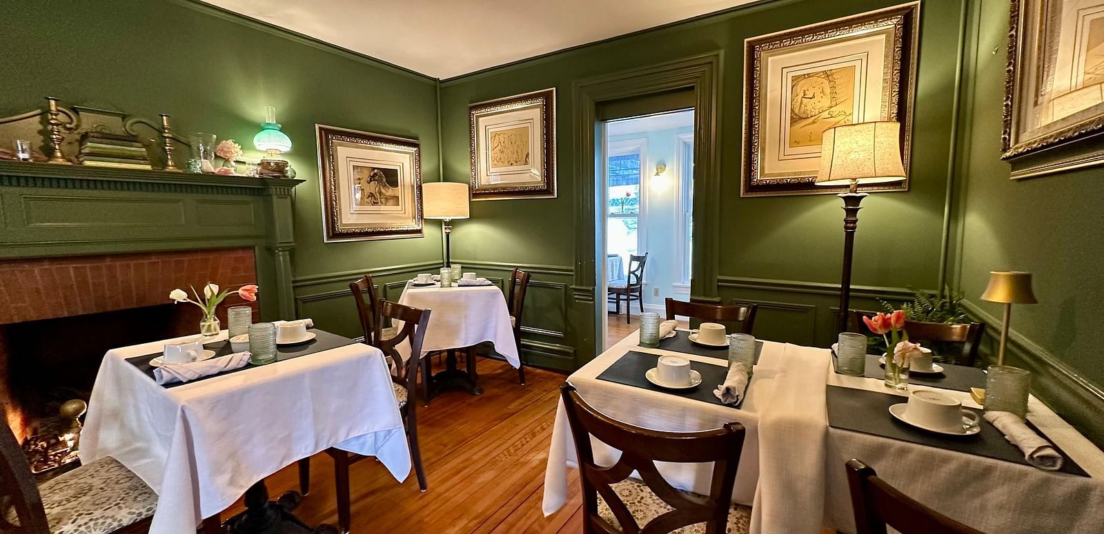 A dining room at Hartstone Inn featuring green walls, white tablecloths, and framed artwork