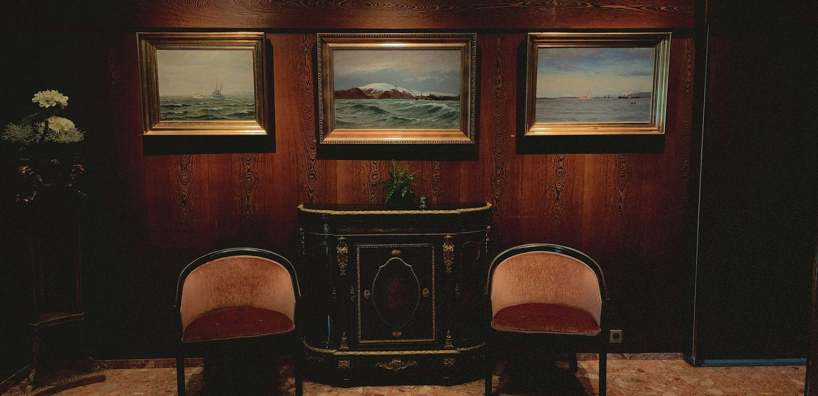 Cozy hotel lounge with classic wood paneling, two armchairs, and framed artwork above a fireplace.