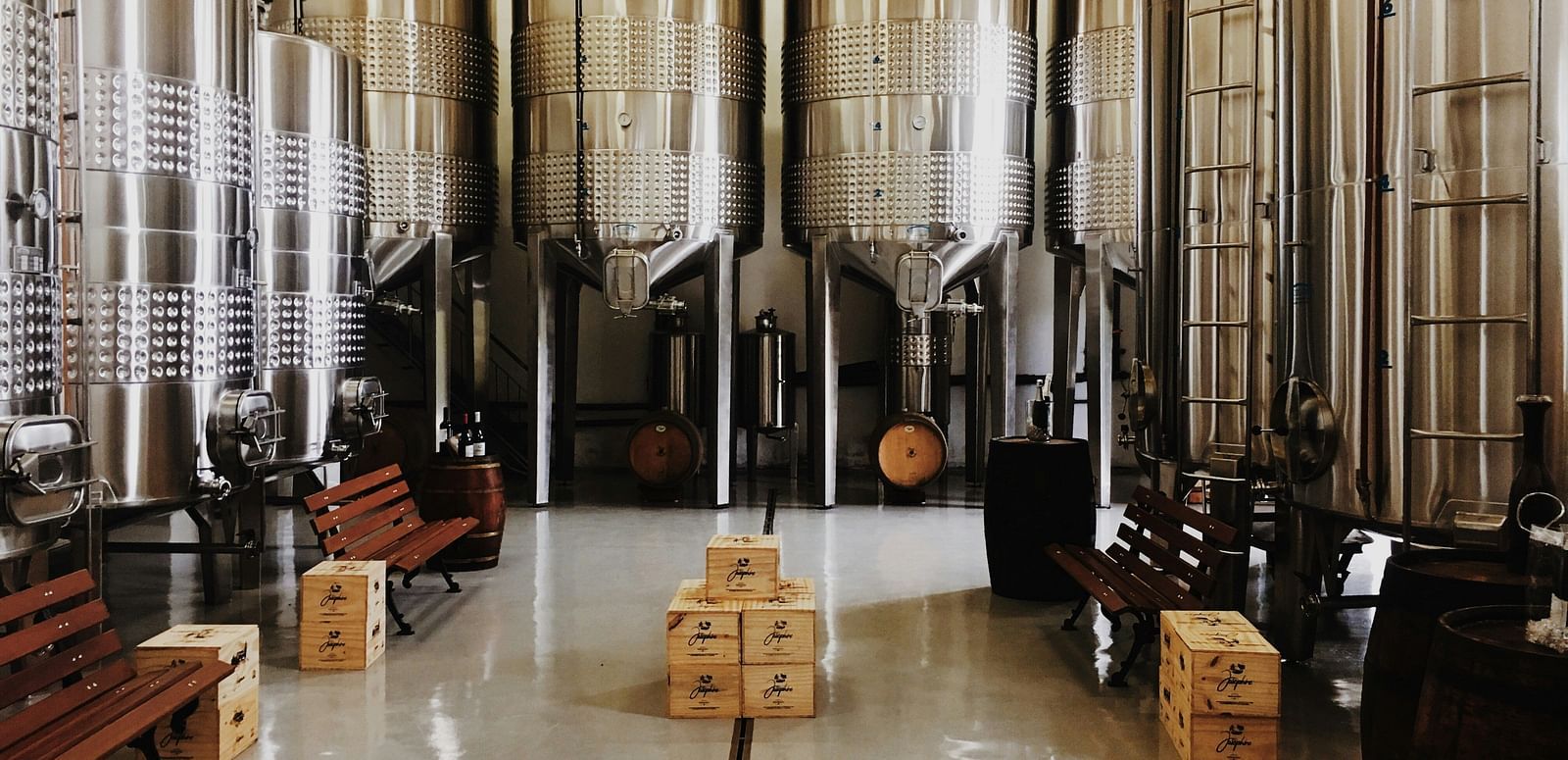 Interior of a winery with large stainless steel fermentation tanks and wine barrels.