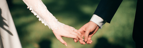 A close-up of a couple holding hands, elegantly dressed in their wedding attire.