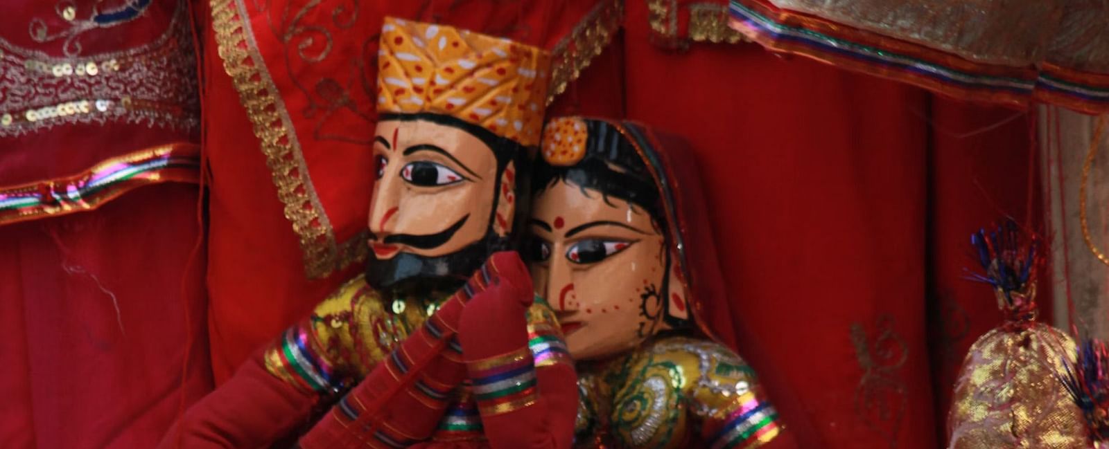 Rajasthani puppets, dressed in traditional attire with intricate details, are displayed against a backdrop of vibrant fabrics.