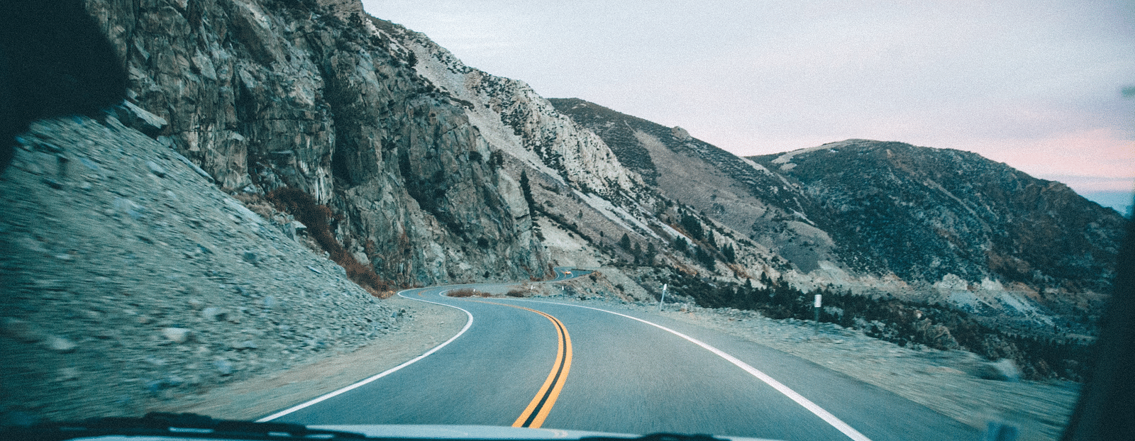 an image captured inside of a vehicle, featuring the road ahead surrounded with the mountain range followed.