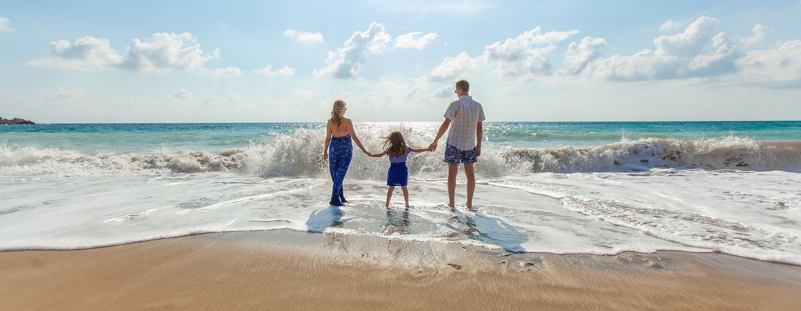 A family holding hands and walking into the waves, enjoying a sunny day at the beach together.