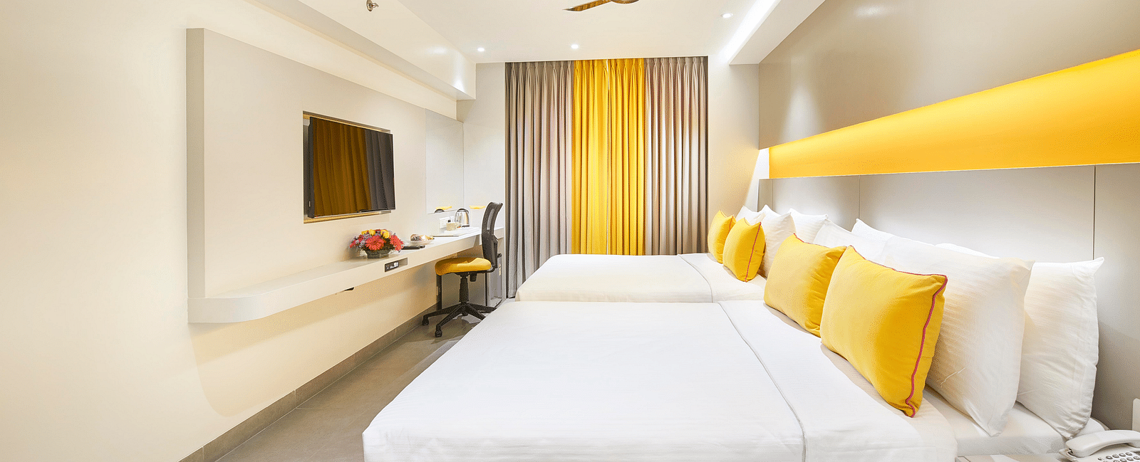  The spacious room has a large bed, a single loveseat beside the bedside table, a wall-mounted television across from it, and a window to the side covered with a curtain