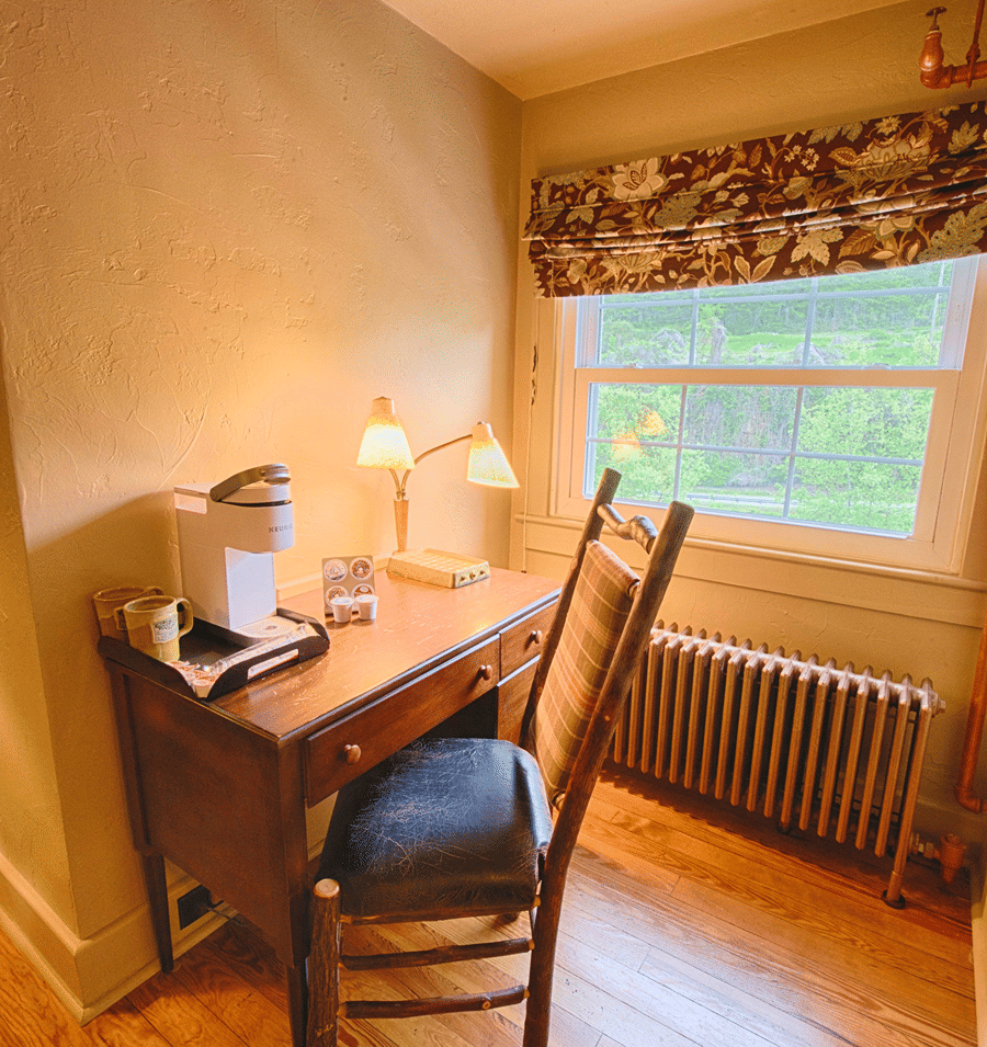 A cozy guest room with a wooden desk, chair, window, and radiator.