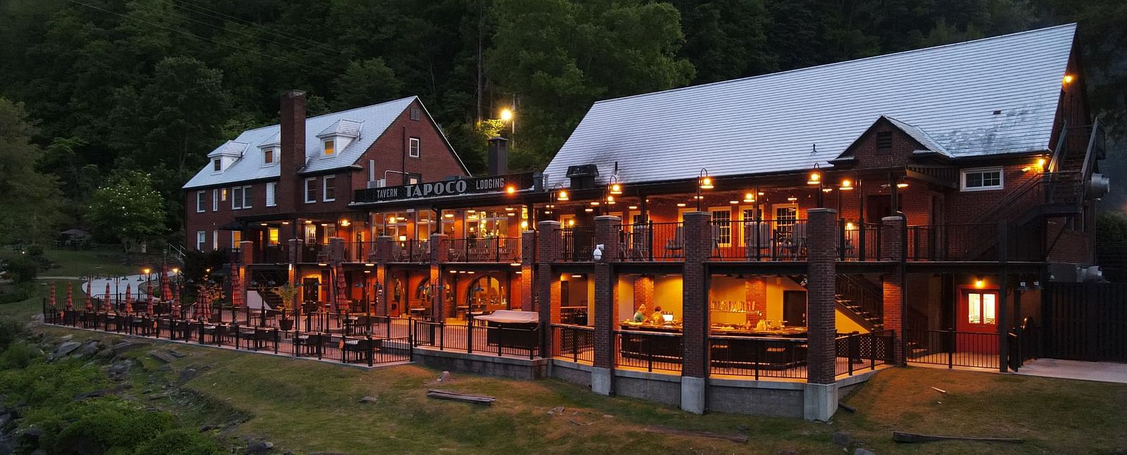 side view of our resort with bright yellow lighting with lush green pine forest in the background - Historic Tapoco Lodge