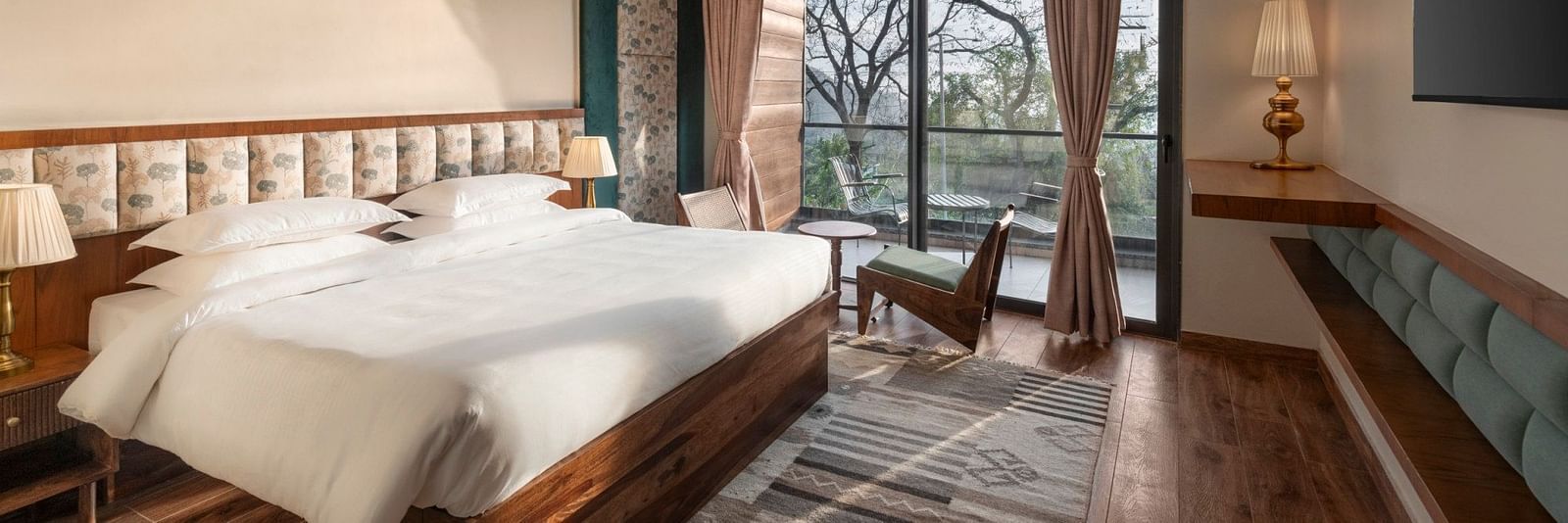A spacious room decorated with a floral pattern headboard, large windows overlooking greenery, and contemporary furniture - The Samai, Bhimtal