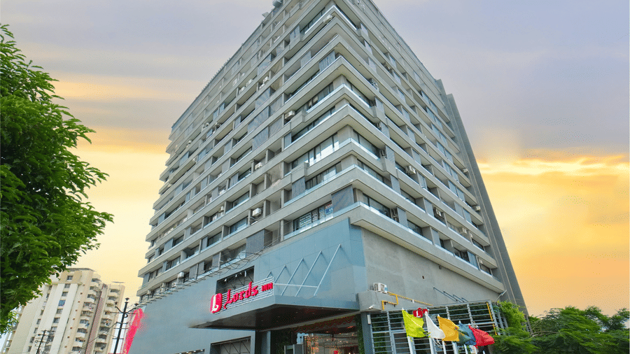 The exterior of the multi-story Lords Inn Rajkot building featuring the main entrance and hotel signage during sunset.