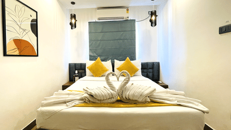 King bed at Hotel Kyzen Smart Stays Madhapur with yellow cushions, swan towel folding, teal headboard panel, framed artwork, and wall-mounted air conditioner above.