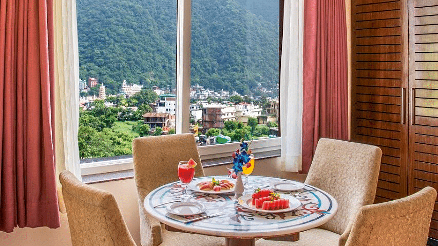 A dining table surrounded with four cushioned chairs overlooking beautiful mountain views from the window of the suite at Regenta Inn DLS.