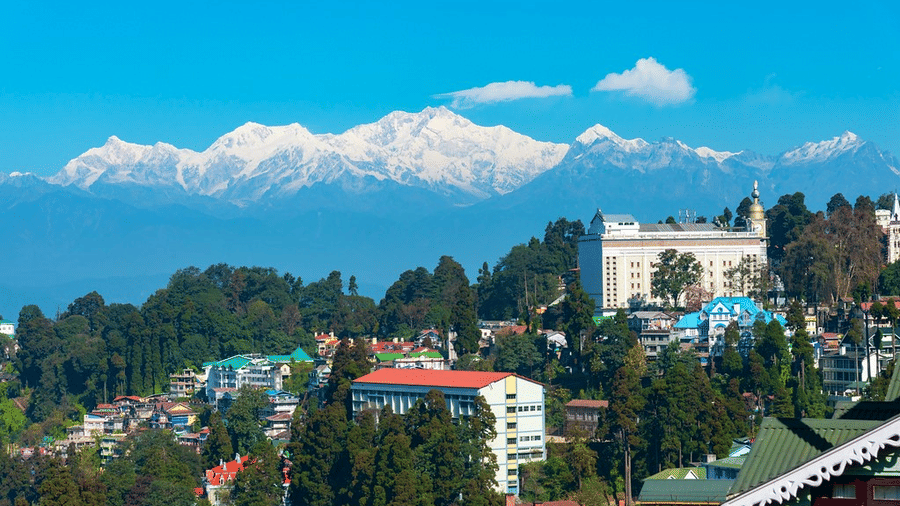 A view of the snow-capped Kanchenjunga mountain range towering over a hillside town Darjeeling, under a clear blue sky.