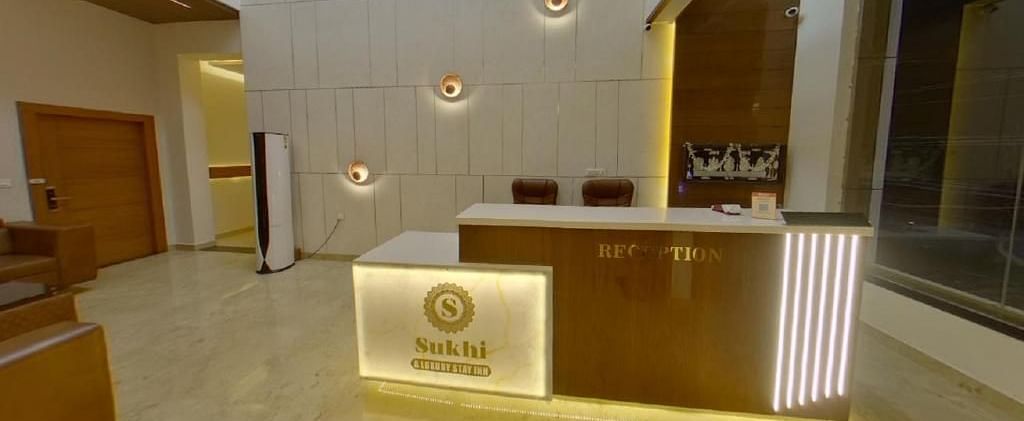 Reception area with a wooden desk featuring an illuminated logo, set against a backdrop of textured walls and ambient lighting.- Sukhi - A Luxury Stay Inn, Chikkamagaluru
