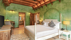 Guest room at Golden Tulip Goa, Mandrem Beach with a 4-poster king bed, green lime-washed walls, a flat-screen TV, and an en-suite bathroom view.