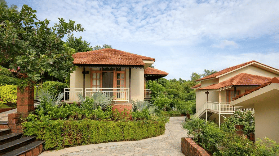 A paved pathway lined with well-trimmed green bushes and trees leading to the villa buildings - Golden Tulip Goa Mandrem