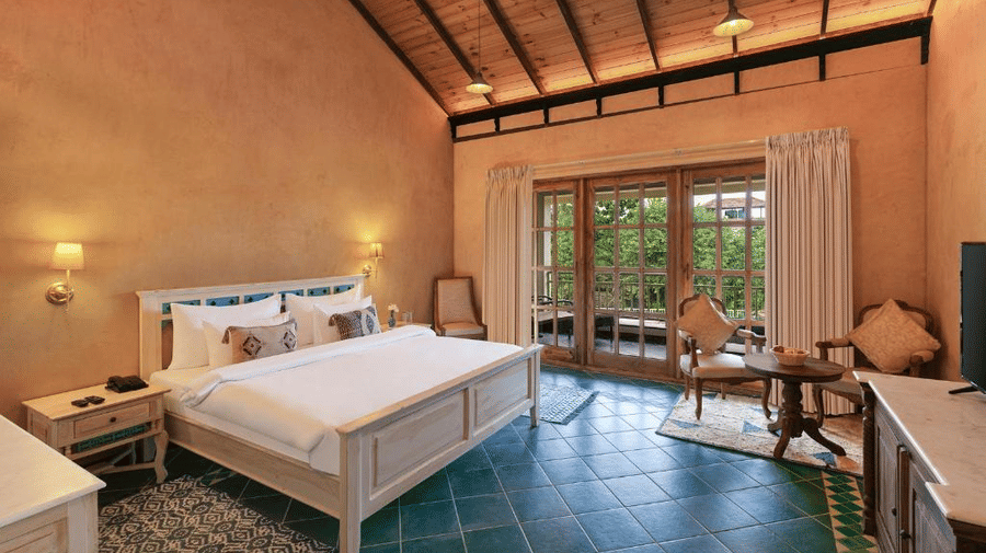 The Premium Room with a private balcony featuring a neatly kept double bed against a rustic wall with 2 bedside lamps mounted on it - Golden Tulip Goa Mandrem