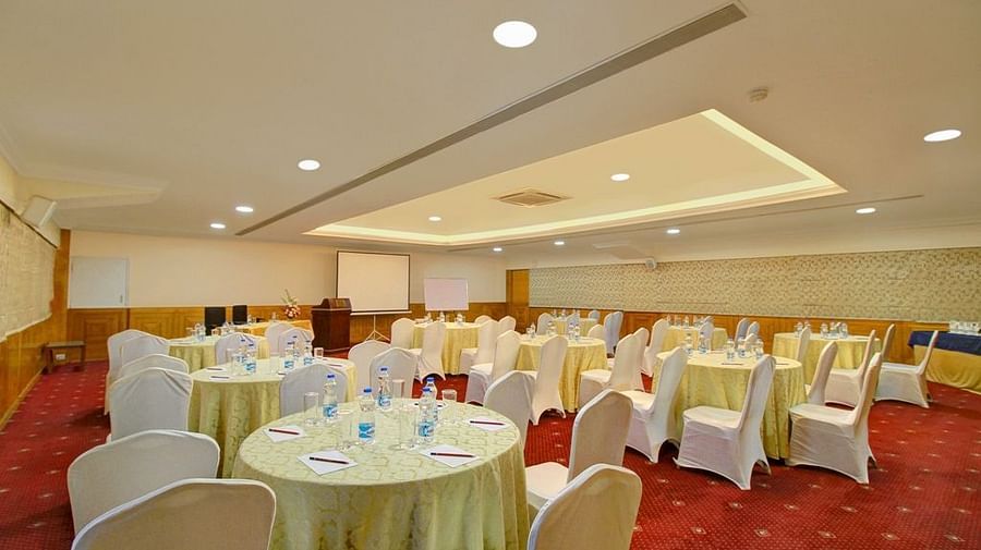 An energetic image of the inside view of a banquet hall showing the chairs and round tables arranged for a conference - Monarch Hotels