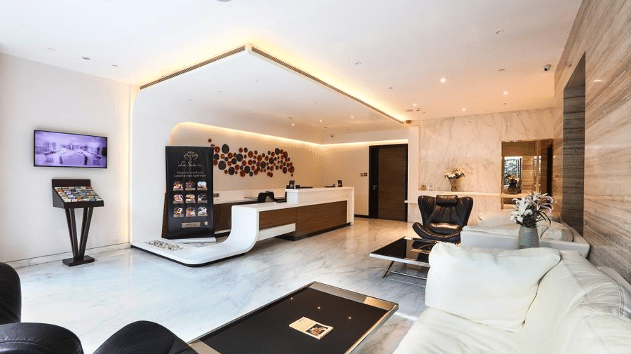 Bright and modern hotel lobby reception area featuring white sofas, a sleek front desk, and recessed warm lighting.