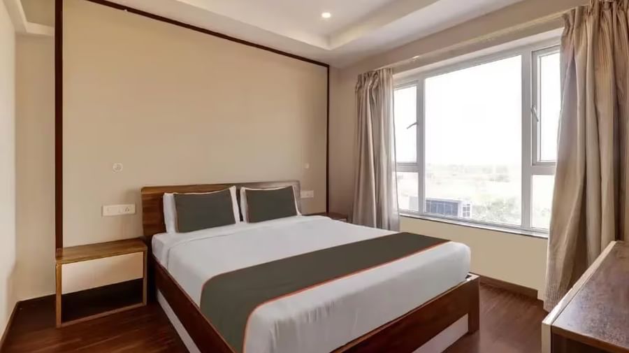 A hotel room with a double bed, dark headboard, and large window with light curtains - VITS Select Kailash Inn, Bagalkot