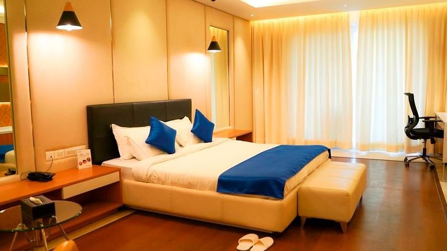A warm and inviting hotel room at BNGV Grandeur Hotel and Banquets, featuring a bed with blue linens, wooden accents, and soft ambient lighting.