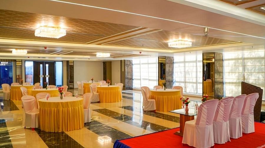 Another view of an elegant event space at BNGV Grandeur Hotel and Banquets, with round tables draped in yellow and white, and red chairs.