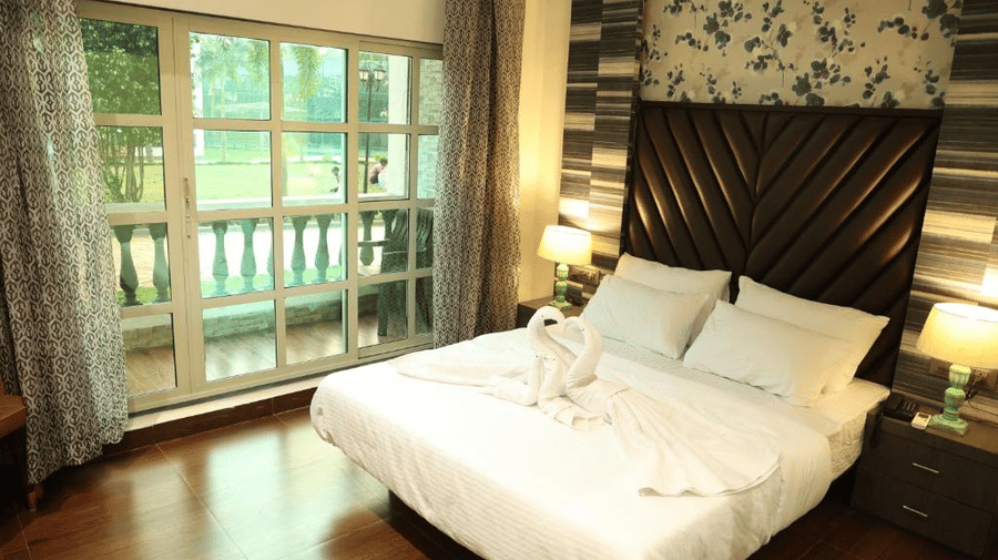 Elegant master bedroom featuring a tall cushioned headboard, floral wallpaper, and a private balcony - DAN Resorts & Weddings, Palghar