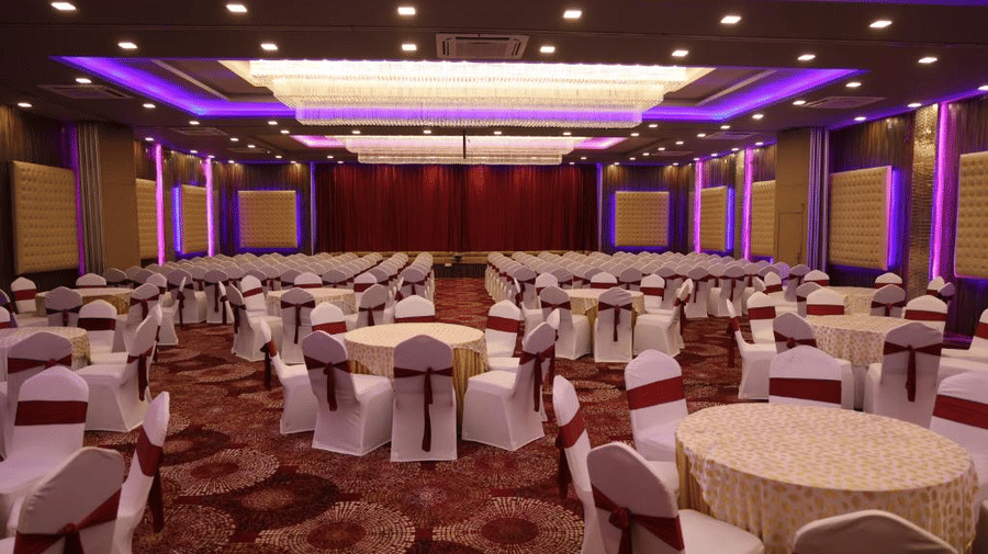 Elegant banquet hall set up with round tables, white chair covers, and purple ambient lighting - DAN Resorts & Weddings, Palghar