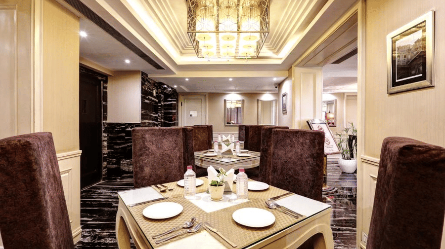 A square wooden dining table meticulously set with white plates and glassware, surrounded by tall chocolate-brown velvet chairs - Flute Boutique By Hotel 91, Jaipur