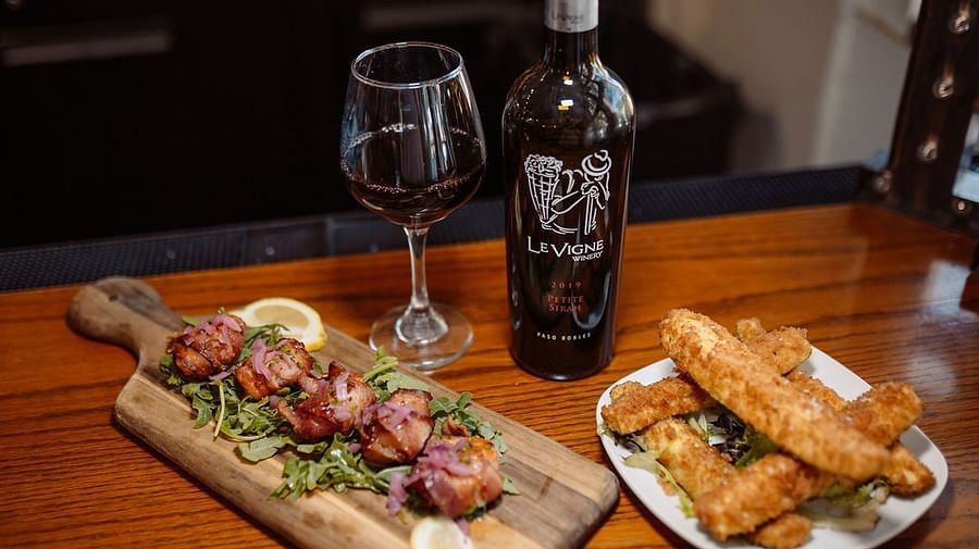 Two dishes being served alongside a bottle of red wine on a wooden table - Narrow Gauge Inn - A Serenite Hotel Near Fish Camp.