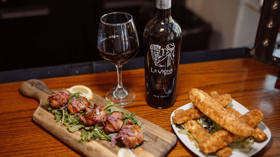 Two dishes being served alongside a bottle of red wine on a wooden table - Narrow Gauge Inn - A Serenite Hotel Near Fish Camp.