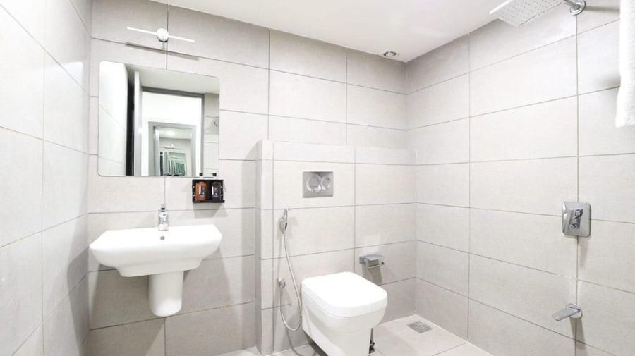 A bathroom with white tiles all around featuring wash basin along with a commode and a shower area at Pravasa Ahmedabad.