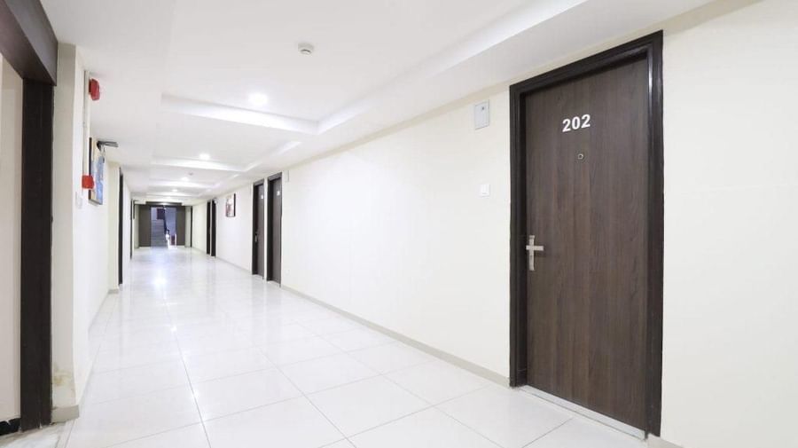 A side-angle view of the corridor featuring dark brown doors of the rooms awith room numbers written on them at Pravasa Stay, Ahmedabad (Alba Premier).