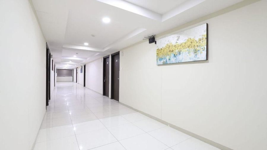 A brightly-lit corridor with false ceiling and a landscape painting mounted on the wall at Pravasa Stay, Ahmedabad (Alba Premier).